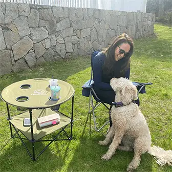 woman in camp chair next to camp table and a dog