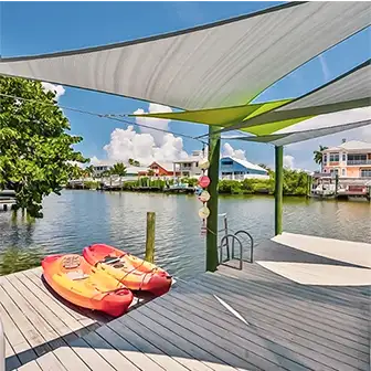 shade sails hung over a dock. 2 canoes are on one of the decks.